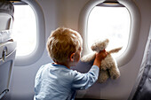 Junge schaut mit Teddybär aus einem Flugzeugfenster, Flughafen Singapur, Singapur