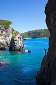 Frau springt vom Felsen ins Meer an der Bar La Grotta, La-Grotta-Bay, bei Paleokastritsa, Insel Korfu, Ionische Inseln, Griechenland