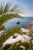 Palm fronds, parasols and excursion boat near the coastline, Dubrovnik, Dubrovnik-Neretva, Croatia