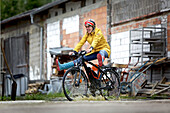 Junge Frau fährt mit einem elektrischen Fahrrad durch eine Pfütze, Tanna, Thüringen, Deutschland