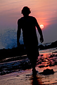 Mann geht am Strand im Sonnenuntergang entlang, Jakarta, Java, Indonesien