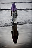 Girl wearing traditional clothes standing in water at beach, Jakarta, Java, Indonesia