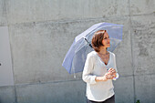Frau steht mit einem Schirm vor einer Betonmauer, München, Bayern, Deutschland
