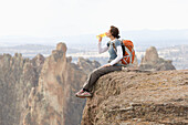 A woman with a day pack and water bottle sits on the edge of a steep cliff Terrebone, Oregon, USA