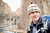 A male rock climber with a wool hat smiling with cliffs in the distance Terrebone, Oregon, USA