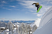 A snowboarder launching into fresh powder snow with mountains and blue sky in the background Squaw Valley, California, USA