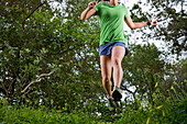 View from below of a woman trail running through a green meadow in the woods Montecito, California, USA