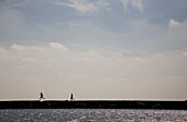 Two young people run on a pier overlooking the ocean (silhouette) Galveston, Texas, USA