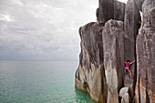 A woman climbs a granite rock pillar over the ocean on Coombe Island, Queensland, Australia Queensland, Australia