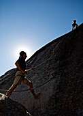 A young man leads a rock climb, while another young man belays him, in Yosemite, California Yosemite, California, USA