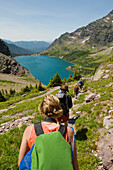 A group of backpackers hike down a trail towards an alpine lake, Glacier National Park, Montana Montana, USA