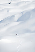 A skier makes his way down an alpine run to a waiting helicopter in the Selkirk Mountains, Canada British Columbia, Canada