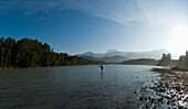 A man in waders casts into a river while fly fishing in Squamish, British Columbia Squamish, British Columbia, Canada