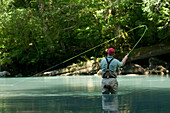 A man wearing waders stands in a river while fly fishing in Squamish, British Columbia Squamish, British Columbia, Canada