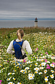 A woman hiking through wildflowers towards a lighthouse, IIwaco, Washington Ilwaco, Washington, USA