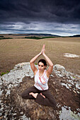 A woman practices yoga in a field under cloudy skies in Brazil Brazil