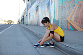 A female runner sits by the side walk on a street in San Diego, California and ties her shoes San Diego, California, USA