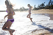 Two pre-teen girls running to the water at Paia Beach, Maui, Hawaii smile as they get wet Maui, Hawaii, USA