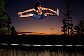 A professional slackliner plays around on the slackline in a field at sunset in the Blue Mountain of Missoula, Montana Missoula, Montana, USA