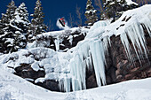 A snowboarder jumps off an ice waterfall cliff into powder in Colorado Vail, Colorado, USA