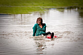 A young women laughs while sitting in a large puddle Sandpoint, Idaho, USA