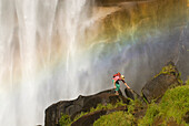 A young woman explores beneath a giant waterfall CA, USA