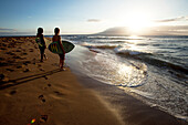 Two men watching the surf at sunset with their skimboards in their arms Ka'anapali, Hawaii, USA