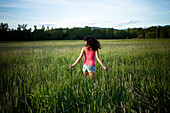 A girl twirls through tall grass on a sunny day in Idaho Sandpoint, Idaho, USA