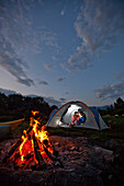 Young adult couple camping with a camp fire and kayaks on a beautiful summer evening Sandpoint, Idaho, USA