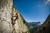 A strong young man climbs a vertical ladder, bolted to the side of a stone cliff and overlooking a valley in the French Alps Mont Blanc, France