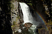A young man rappels down a cliff next to a waterfall and rainbow in Idaho Sandpoint, Idaho, USA