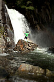 A young man holds his arms open standing at the base of a waterfall after rappeling down Sandpoint, Idaho, USA