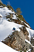 A man makes a turn above a large cliff in the Wasatch Backcountry Utah, USA