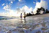 A couple walking along the beach in the sunrise in Hawaii north shore of Oahu, Hawaii, USA