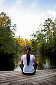 young woman relaxing on a pier looking out over a canal towards the distant trees, Niceville, Florida, United States