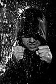 A young man wearing a hooded jacket poses in a wushu stance while it rains down on him Camarillo, California, United States of America
