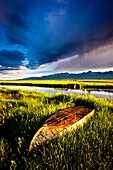 Boat in green grass with pond, mountains and stormy sky.  Westcliffe, Colorado Westcliffe, Colorado, United States