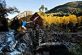 A young man walks a high line with glowing leaves and a raging river below Crystal, Colorado, USA