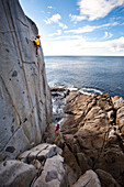 Male climber in a yellow shirt nearing the top of a sea cliff in Tasmania Tasmania, Australia