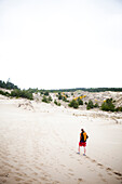 A girl walks alone on the sand dunes wearing a backpack Oregon, USA