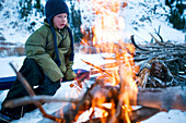 A boy enjoys the warmth of the fire in the backcountry of California Sierra, CA, USA