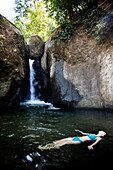 A woman floats on her back while swimming in a pool of water with a waterfall Ojochal, Costa Rica