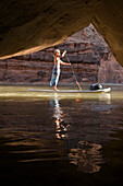 Woman on paddle board in front of cave while rafting down the Lower San Juan River, Mexican Hat, Colorado Mexican Hat, Utah, USA