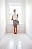 young girl looks out window in white room, Portland, Maine, USA