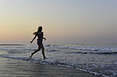 A young woman runs in the surf during sunset Massachusetts, USA