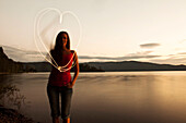 A young woman drawing a heart at sunset next to a lake in Idaho Sandpoint, Idaho, USA