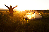 A man standing next to his tent at sunset on a backpacking trip in the mountains of Montana Bozeman, Montana, USA