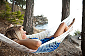 A beautiful young women smiling while sitting in a hammock next to a lake in Idaho., Sandpoint, Idaho, USA