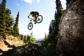 A athletic man mountain biking jumps off a large cliff while downhilling in Wyoming., Jackson, Wyoming, USA