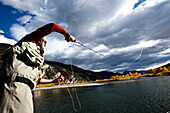 A fly fisher casting his line out of a boat while fly fishing surrounded by fall colors in Montana., Bozeman, Montana, USA